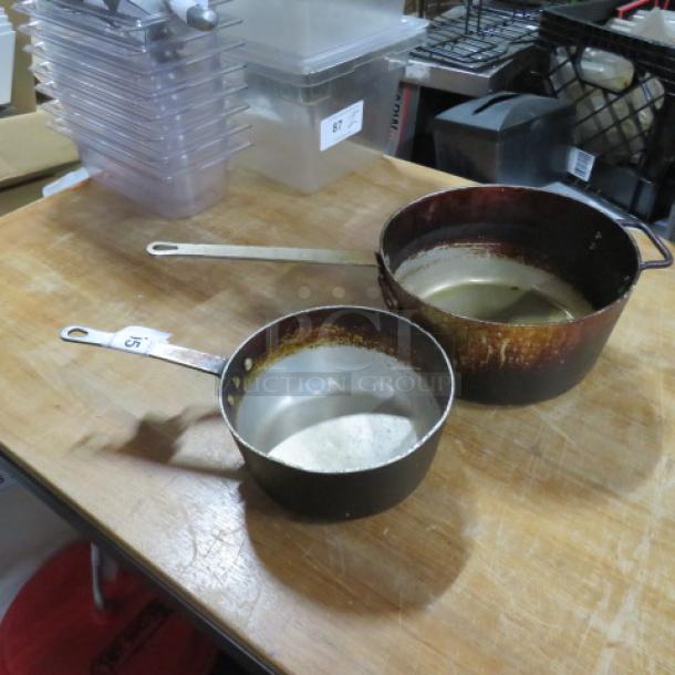 Assorted size sauce pots, showing wear. Includes two metal pots with long handles. Ideal for kitchen use.