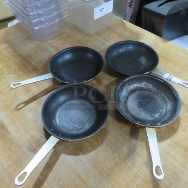 Four 8-inch sauté pans with metal handles, showing signs of use. Ideal for cooking enthusiasts or restaurants.
