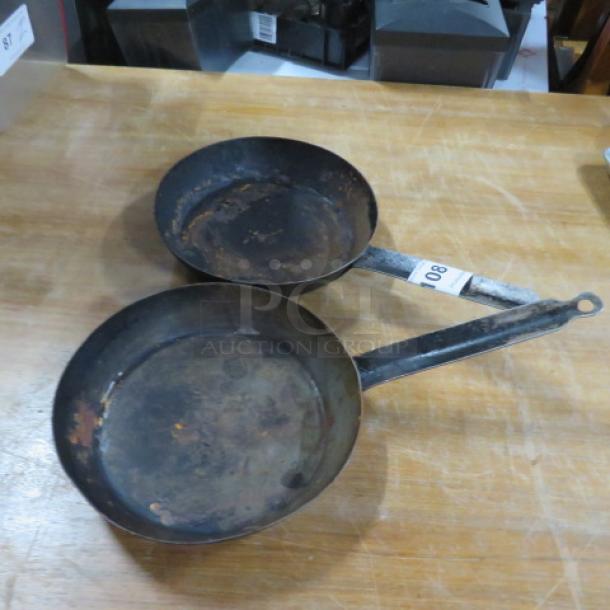 Two vintage 9.5-inch sauté pans, both with visible wear and patina. Handles attached; auction tag reads "008."