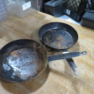 Two used sauté pans with noticeable wear and rust on surfaces, one marked as 11 inches, placed on a wooden countertop.