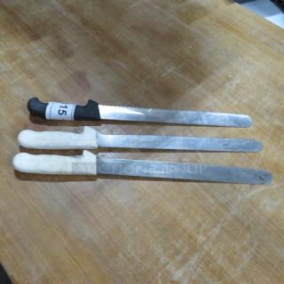 Assorted chef knives, including two with white handles and one with a black handle, marked "151," on a wooden surface.