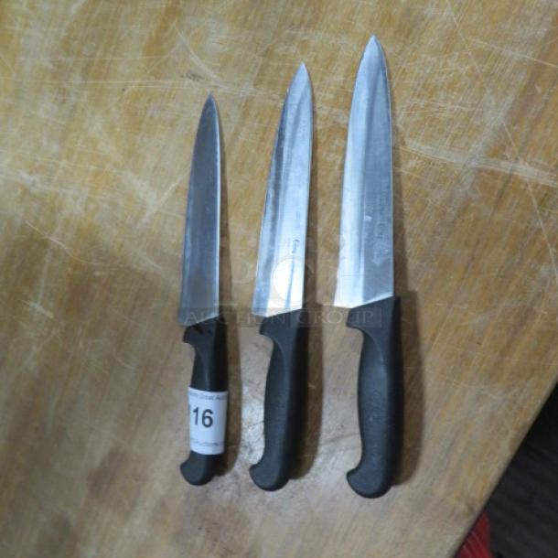 Three assorted chef knives on a wooden surface, black handles, varying blade lengths, each in good condition. Label marked "16."