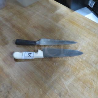 Two assorted chef knives on a wooden surface, featuring black and white handles; one knife labeled "18."