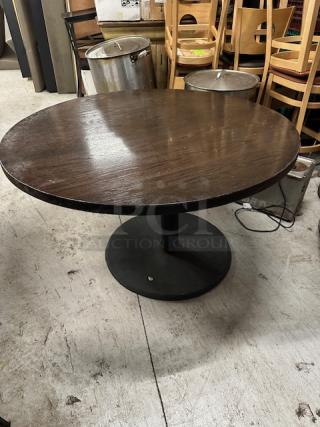 Round solid wood table on a black pedestal base, 48x30 inches. Dark wood finish, good condition, ideal for dining spaces.