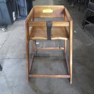 Wooden high chair with safety straps, worn finish. Features a warning label on the backrest. Sturdy construction.