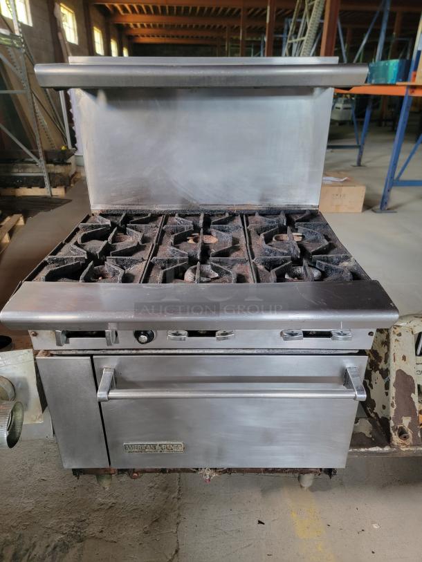 Commercial stainless steel American Range stove with six burners and oven. Used condition, visible wear. Brand label on front.