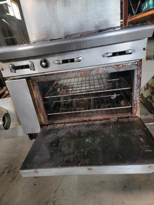 Vintage commercial stove with oven, metal finish, rusted interior, exposed wire racks, and control knobs, showing signs of wear.