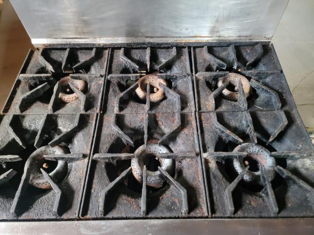 Commercial six-burner gas stove with visible rust and wear, metal grates, and stainless steel backsplash.