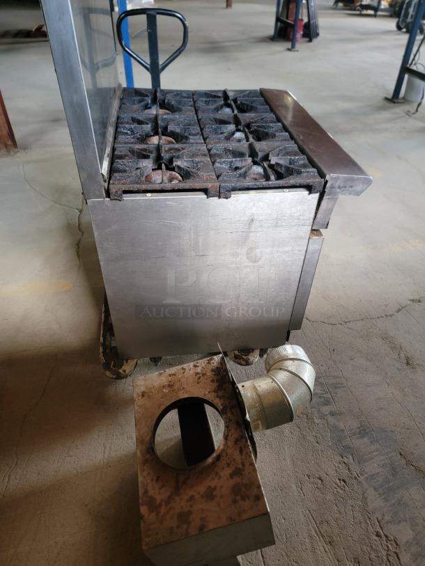 Commercial stainless steel stove with six burners, showing signs of rust and wear, attached vent piece included.