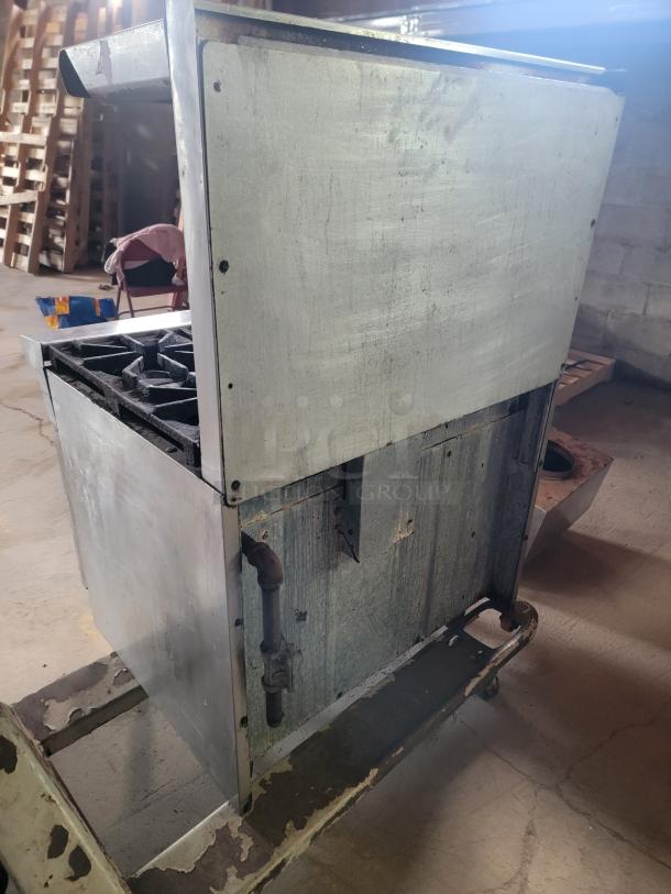 Commercial metal stove with four-burner top, signs of rust and wear, located in an industrial setting.