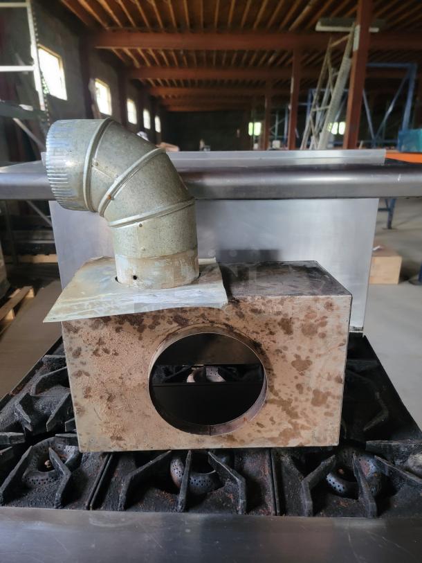 Metal industrial oven hood with ductwork; moderate rust and wear, designed for commercial kitchen use.
