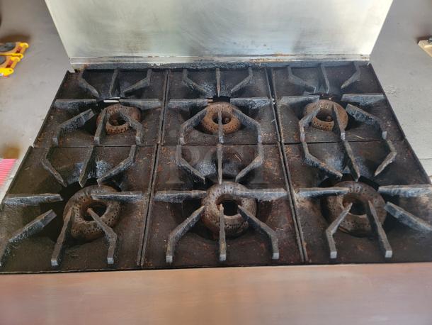 Commercial six-burner gas stove with cast iron grates, showing signs of wear and rust, ideal for restaurant use.