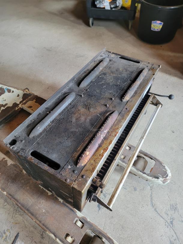 Vintage industrial metal heater, rusted condition, with visible control handle and ventilation grates. No labels or markings.