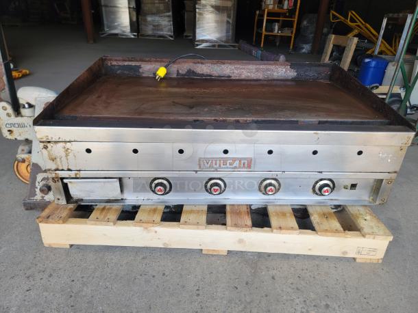 Vulcan commercial griddle with four control knobs, stainless steel finish, showing signs of use, resting on a wooden pallet.