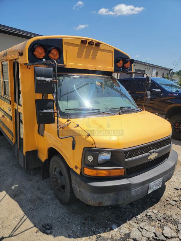 Yellow Chevrolet school bus with visible wear, rust on bumper, and side mirrors. License plate reads “BC-0490.”