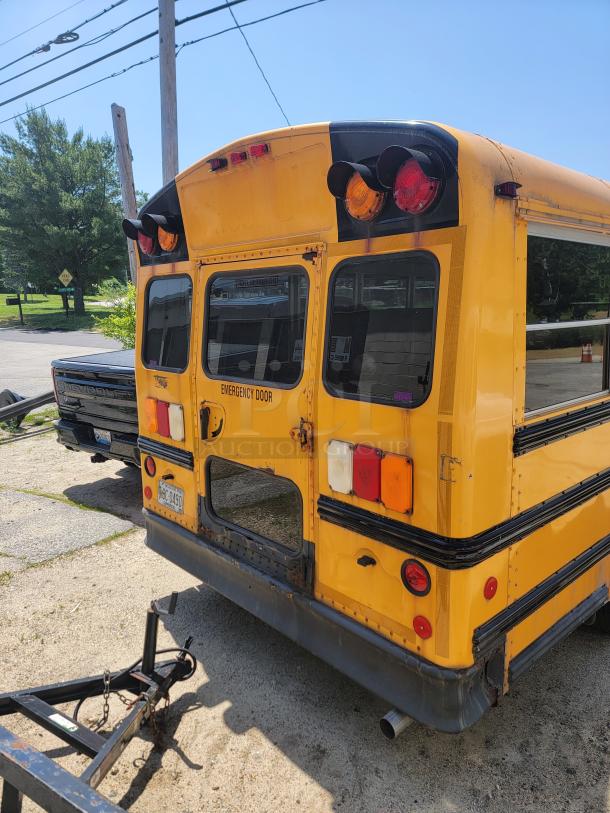Yellow school bus rear with emergency door, visible lights, and some rust. License plate attached. Likely used condition.