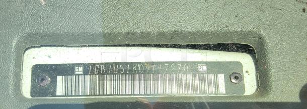Close-up of a General Motors vehicle VIN plate, number 1GBJC31K071172705, affixed to textured surface.