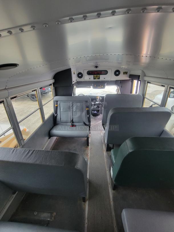 Interior of a used school bus with gray vinyl seats, visible control panel, and seat belts, showing moderate wear.