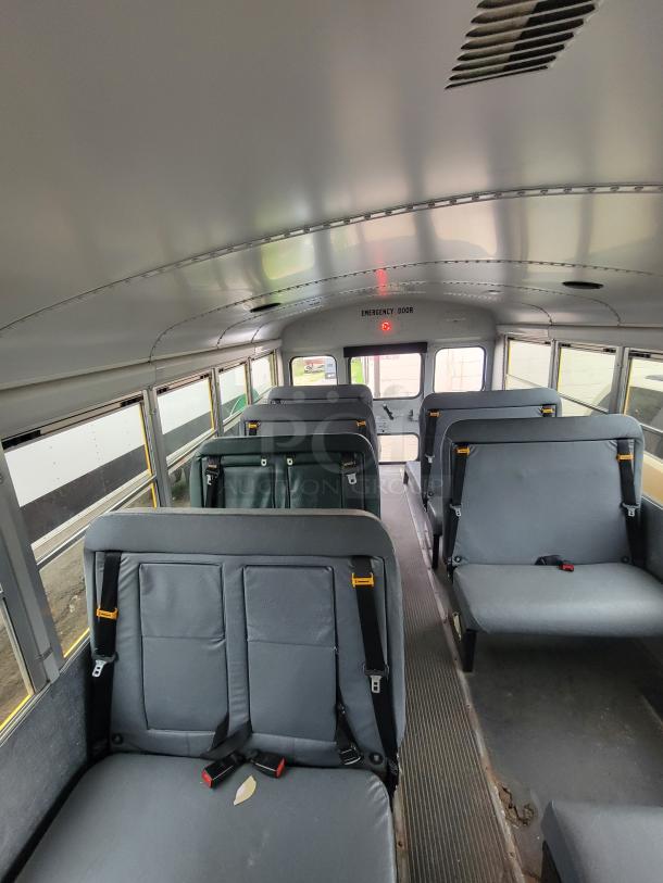 Interior of a school bus showing gray vinyl seats with seatbelts, emergency exit door sign, and visible wear.
