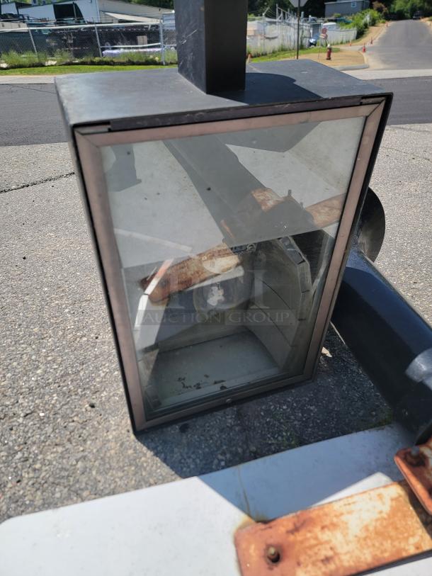 Industrial metal frame mirror with some rust, outdoor setting, shows wear. Reflective surface intact, no visible labels.