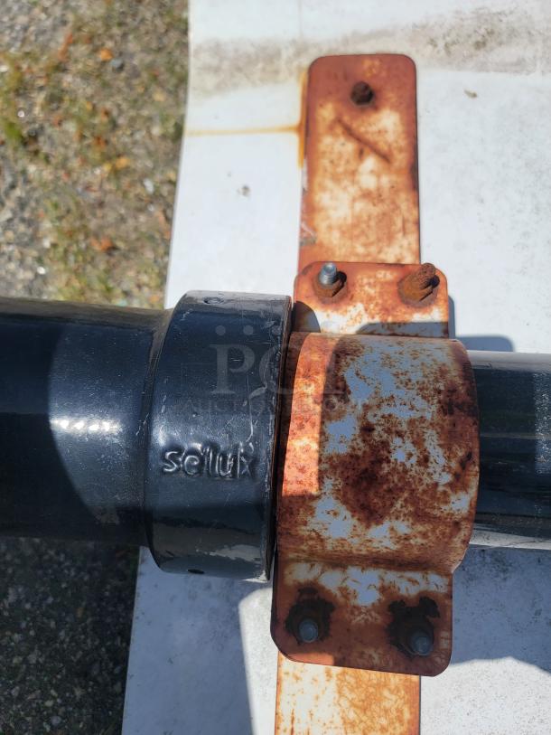 Rusty Selux metal bracket on a black pipe, showing wear and outdoor exposure.