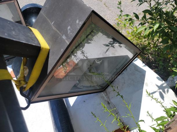 Outdoor lantern with black metal frame and glass panels, showing minor wear. Secured with a yellow strap.
