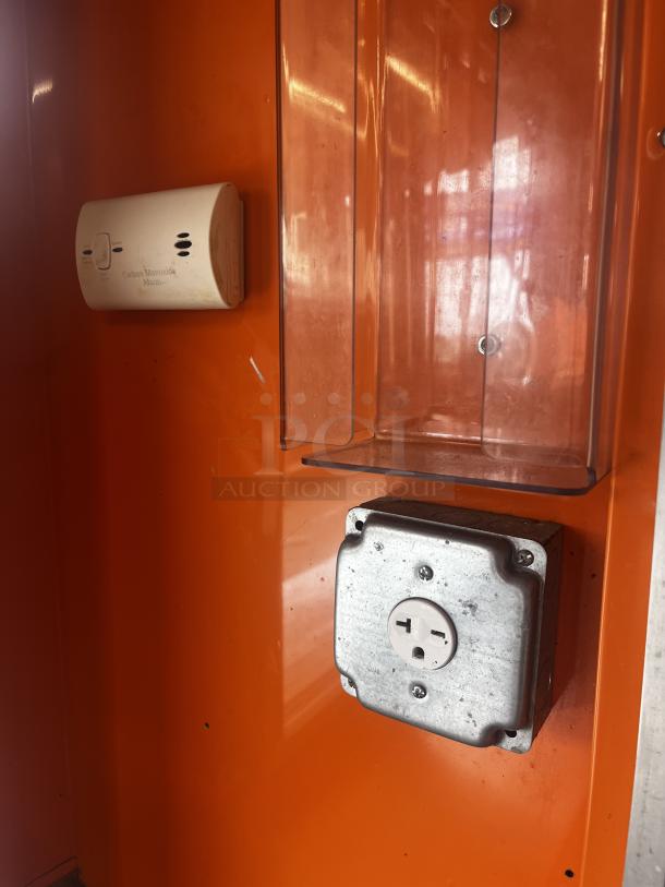 Orange interior of a 2014 Quality Trailers mobile kitchen with a carbon monoxide alarm and an electric outlet.