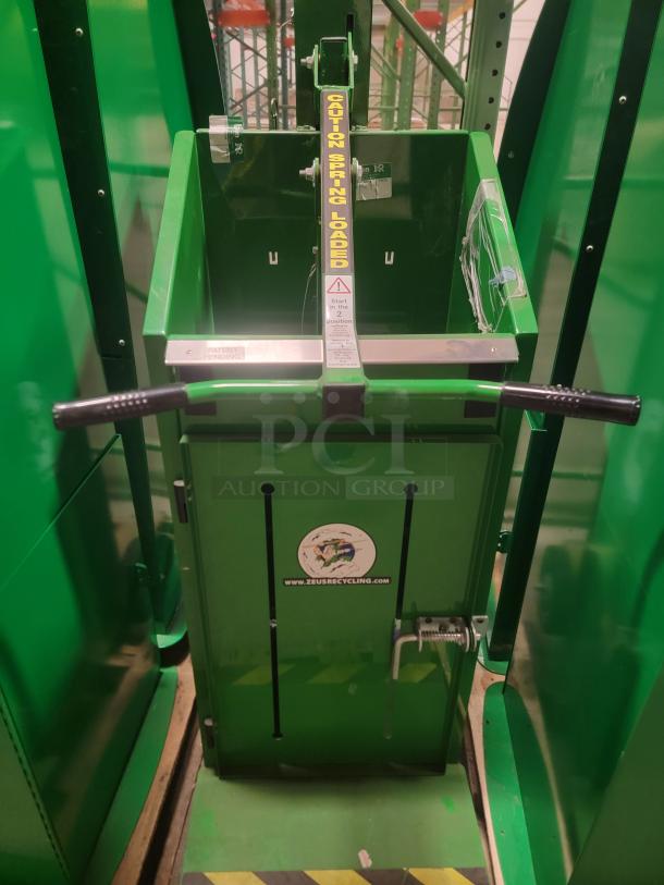 Green Zeus recycling compactor with hand baler. Features "Caution Spring Loaded" label. Ideal for reducing waste in industrial settings.
