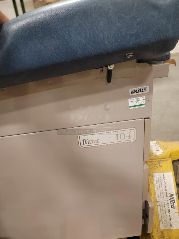 Ritter 104 examination table, heavy-duty design. Features blue upholstery, visible label and sturdy construction. Versatile use.