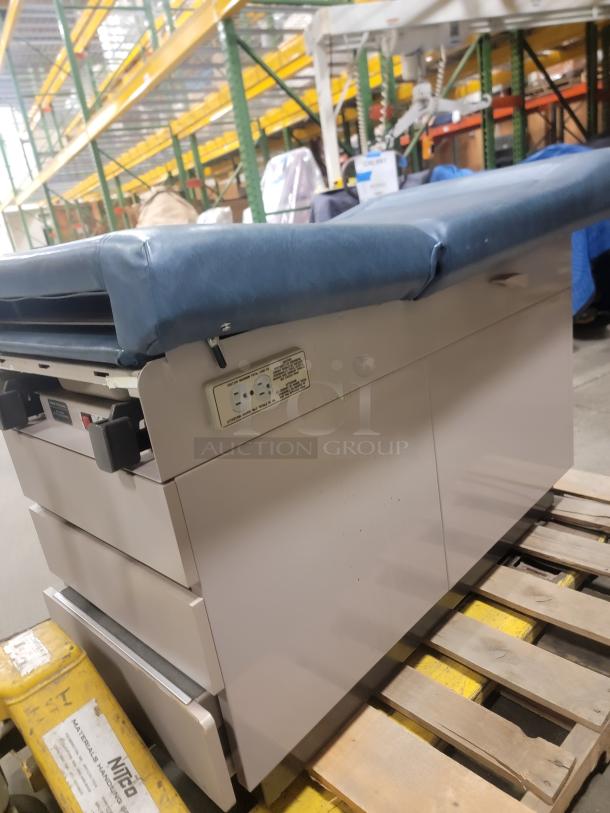 Ritter 104 Exam Table with blue cushioned top, sturdy design, power outlets, and storage drawers. Ideal for versatile uses.