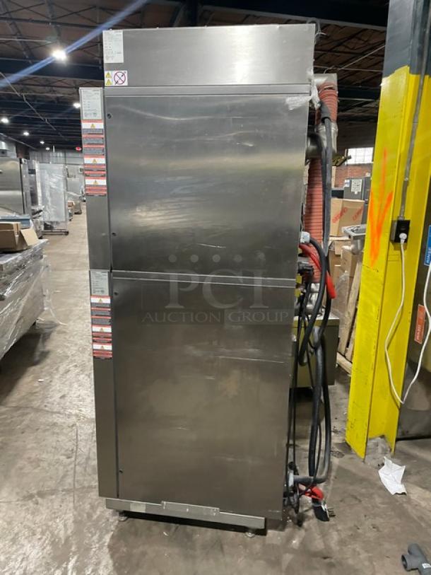 Commercial stainless steel dishwasher with dual doors. Visible safety and operational labels, hose attachments on side.