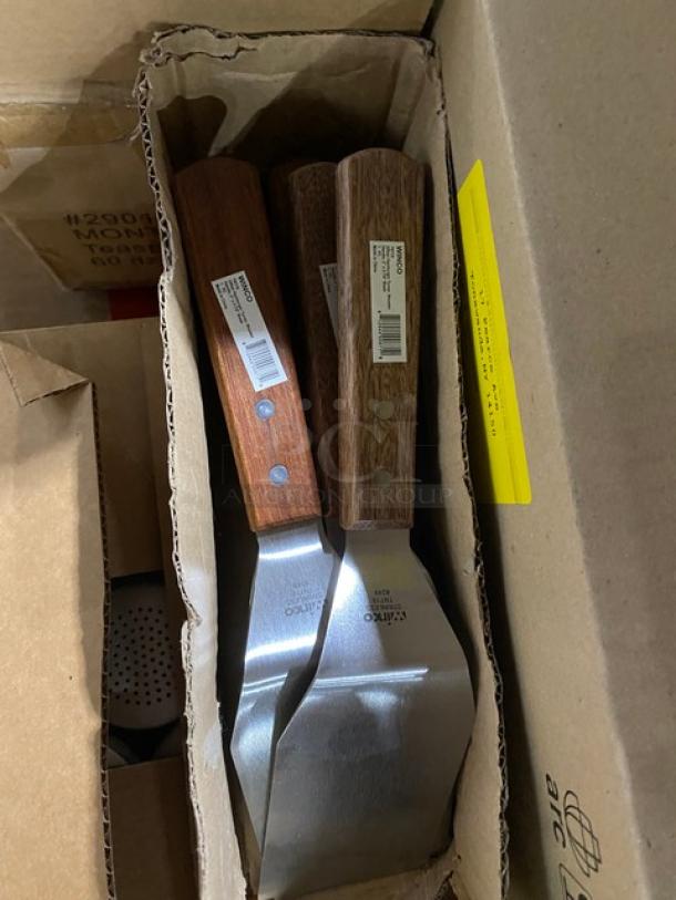 Three metal spatulas with wooden handles in a cardboard box, each with a barcode label, showing robust construction and new condition.