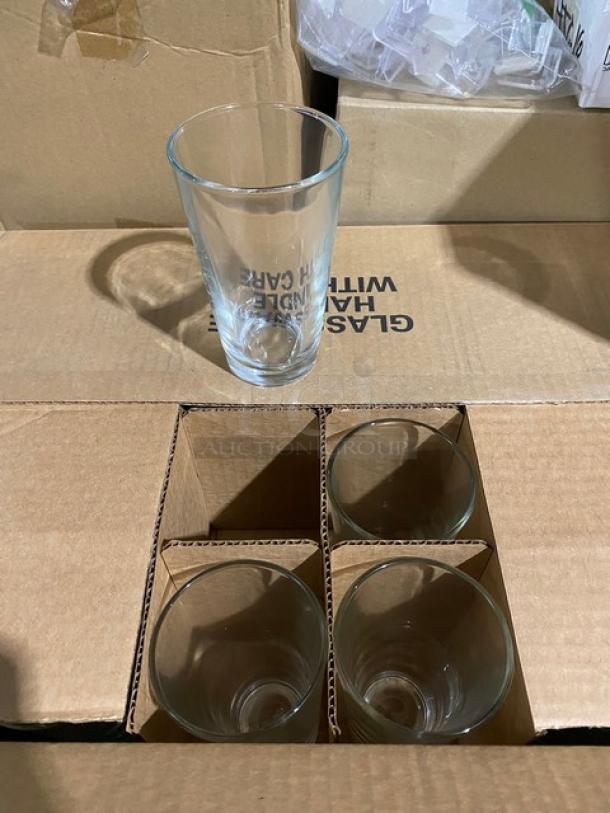 Set of four clear glass tumblers in cardboard box. Visible text: "GLASS HANDLE WITH CARE." New condition.