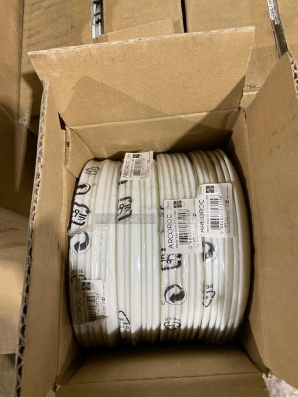 Stack of white Arcoroc plates in a cardboard box, brand labels visible. Plates appear new, showing no signs of use or damage.