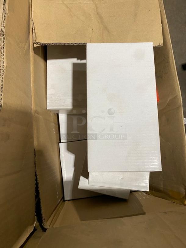 Open cardboard box containing several stacked white rectangular boxes. Boxes appear new, with no visible markings or labels.