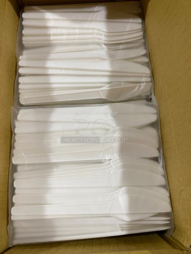Box of white plastic knives stacked in sealed plastic wraps, indicating new condition.