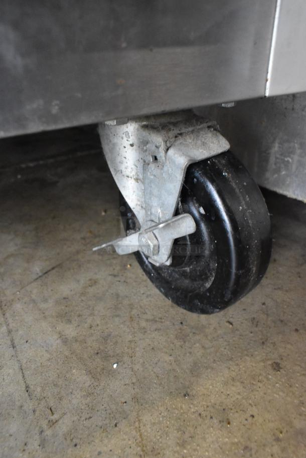 Close-up of a commercial caster wheel on a Traulsen G20010 stainless steel cooler. Visible wear on the surface.