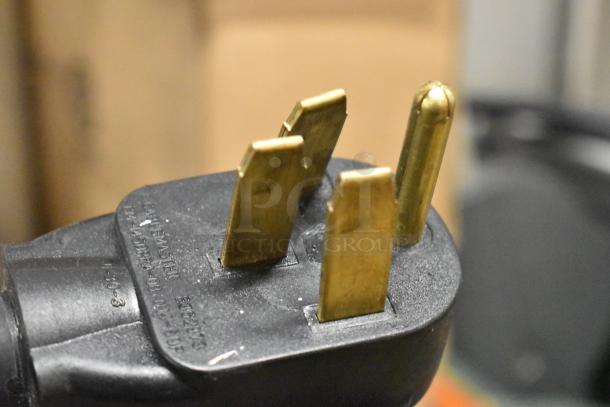 Close-up of a power plug, possibly from the 2020 Bunn ICB TWIN SH coffee machine, showing metal prongs.