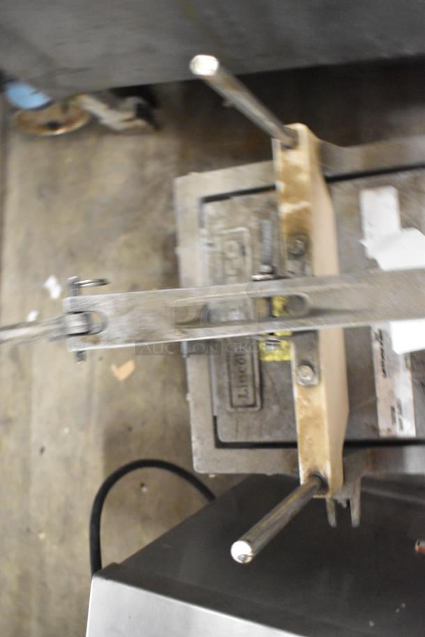 Metal countertop lettuce head cutter with dual handles. Visible wear and sturdy build. Mounted on stainless steel base.