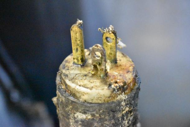 Corroded electrical plug with metal prongs, showing signs of wear and environmental exposure.