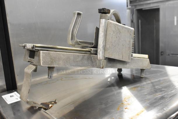 Nemco tomato slicer in used condition, with metal frame and blade assembly, on stainless steel surface. Auction tag visible.