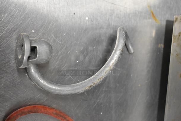 Dough hook attachment in used condition with visible wear, part of a metal food processor set.