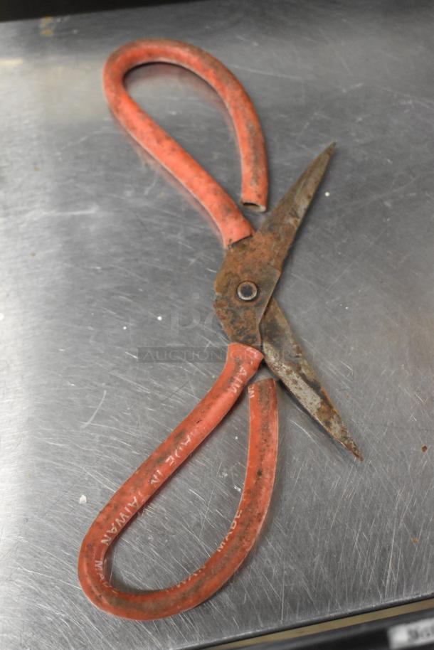 Rusty scissors with red handles, labeled "MADE IN TAIWAN," on a metal surface.
