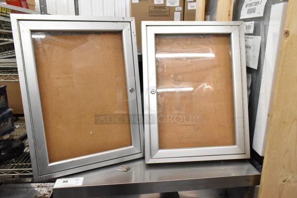 Two large shadowboxes with silver frames, glass fronts, no locking mechanism. Key set visible on shelf. Good condition.