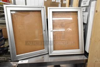Two large shadowboxes with silver frames, glass fronts, no locking mechanism. Key set visible on shelf. Good condition.