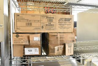 3M Subway Water Filter Cartridge Kit and two Insinkerator Instant Hot Water Tanks in original boxes on metal shelf.