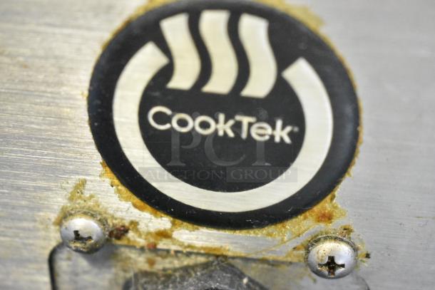 CookTek logo on a metal surface, showing signs of wear around screws and emblem area, indicating brand of induction ranges.