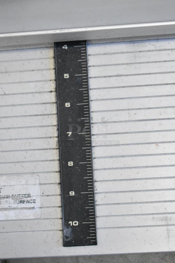 Tile cutter with metal surface and measuring guide, shows signs of wear. Marking indicates use instructions.