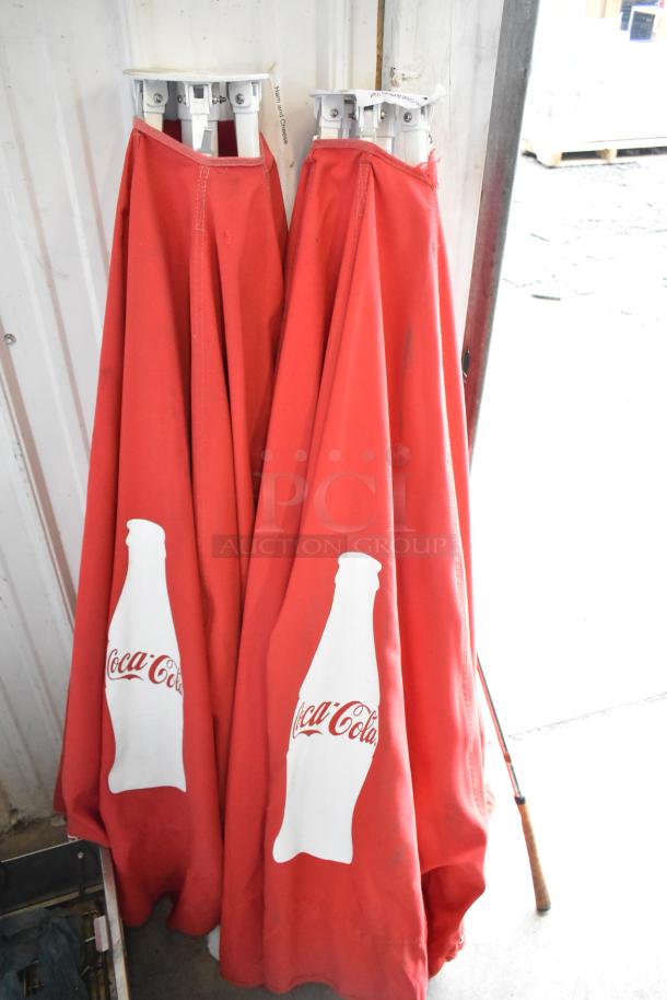 Pair of red Coca Cola patio umbrellas. Features iconic logo. Good condition. Ideal for outdoor use.
