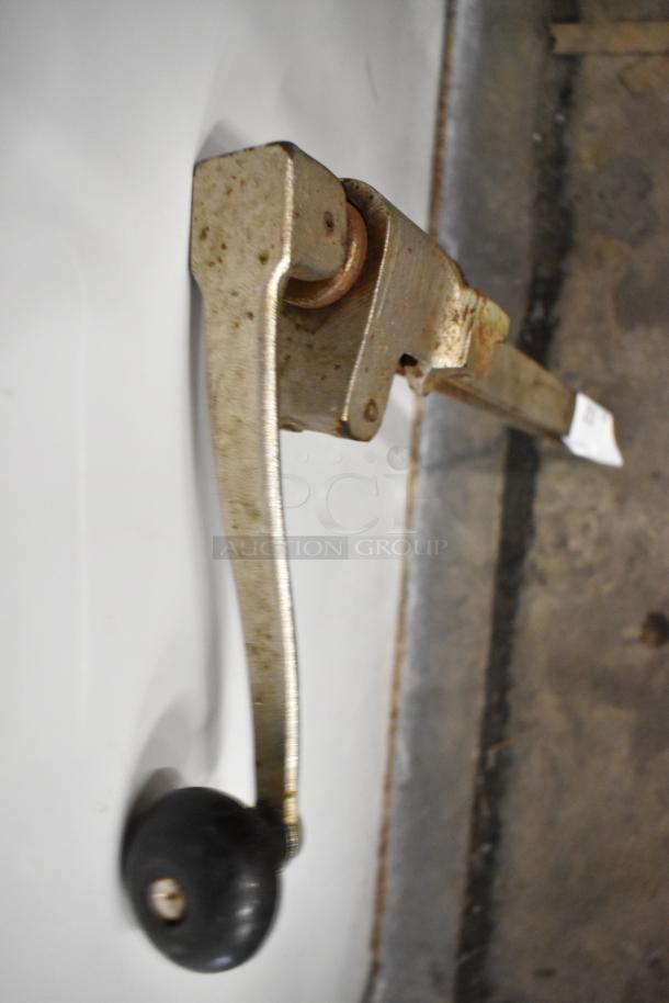 Metal commercial can opener with a long handle and black knob. Shows signs of rust and wear, suitable for heavy-duty use.